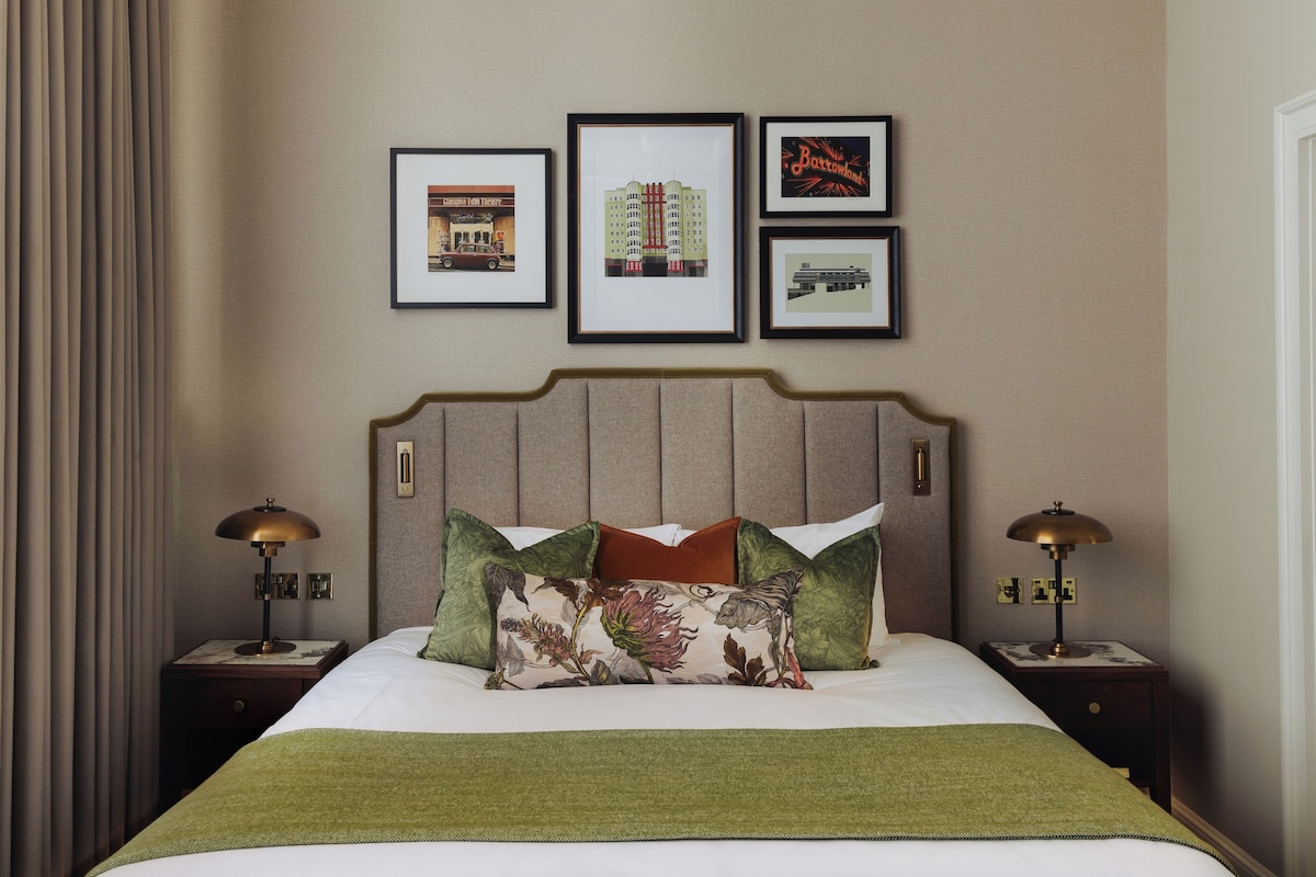 Habitación de hotel con una cama, dos mesitas de noche, un cabecero y tres cuadros enmarcados en la pared.