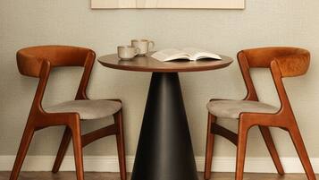 A round table with a black base surrounded by two wooden chairs with cushioned seats.