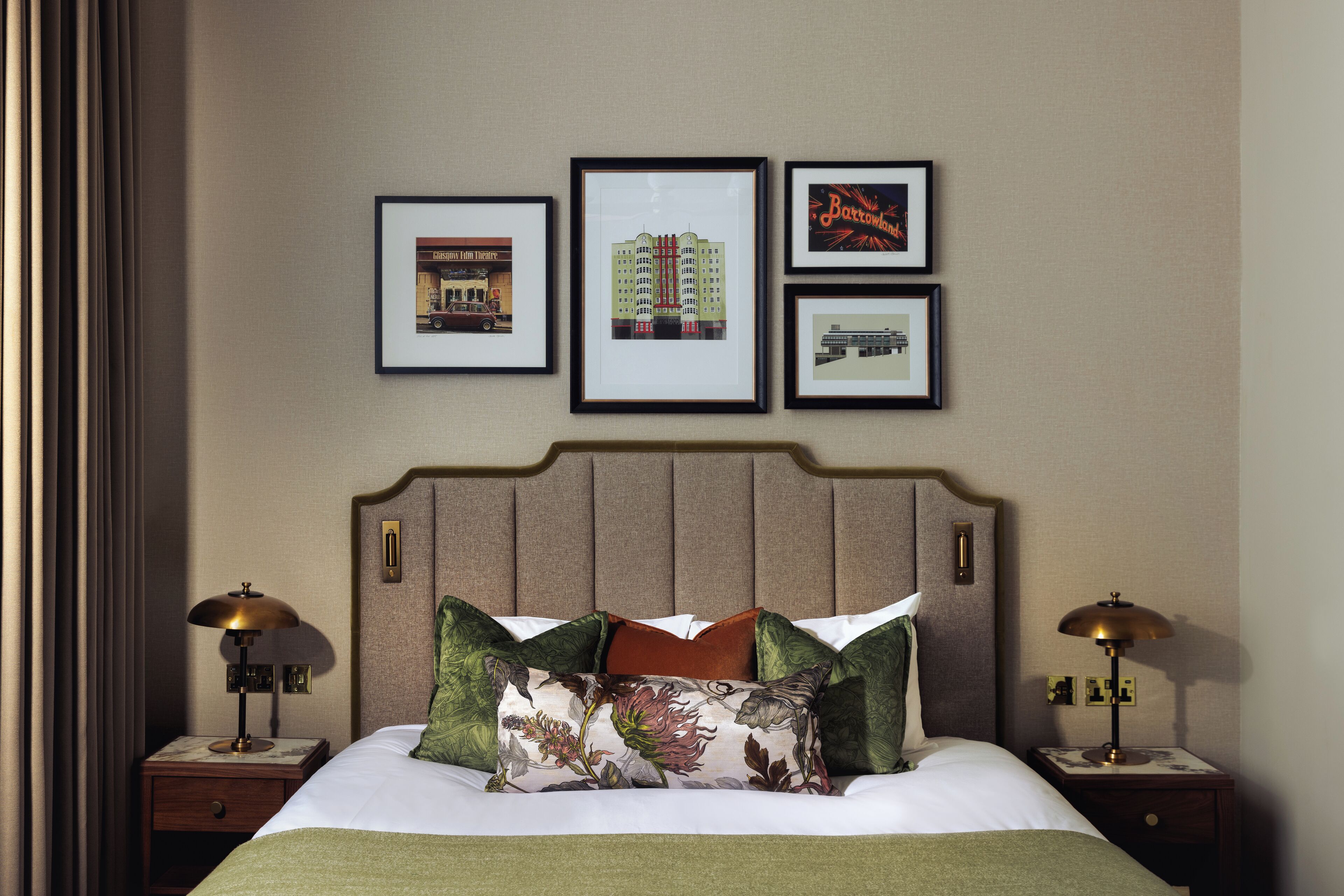 Una cama bien hecha con almohadas florales, un cabecero con reloj integrado y cuadros enmarcados en la pared.