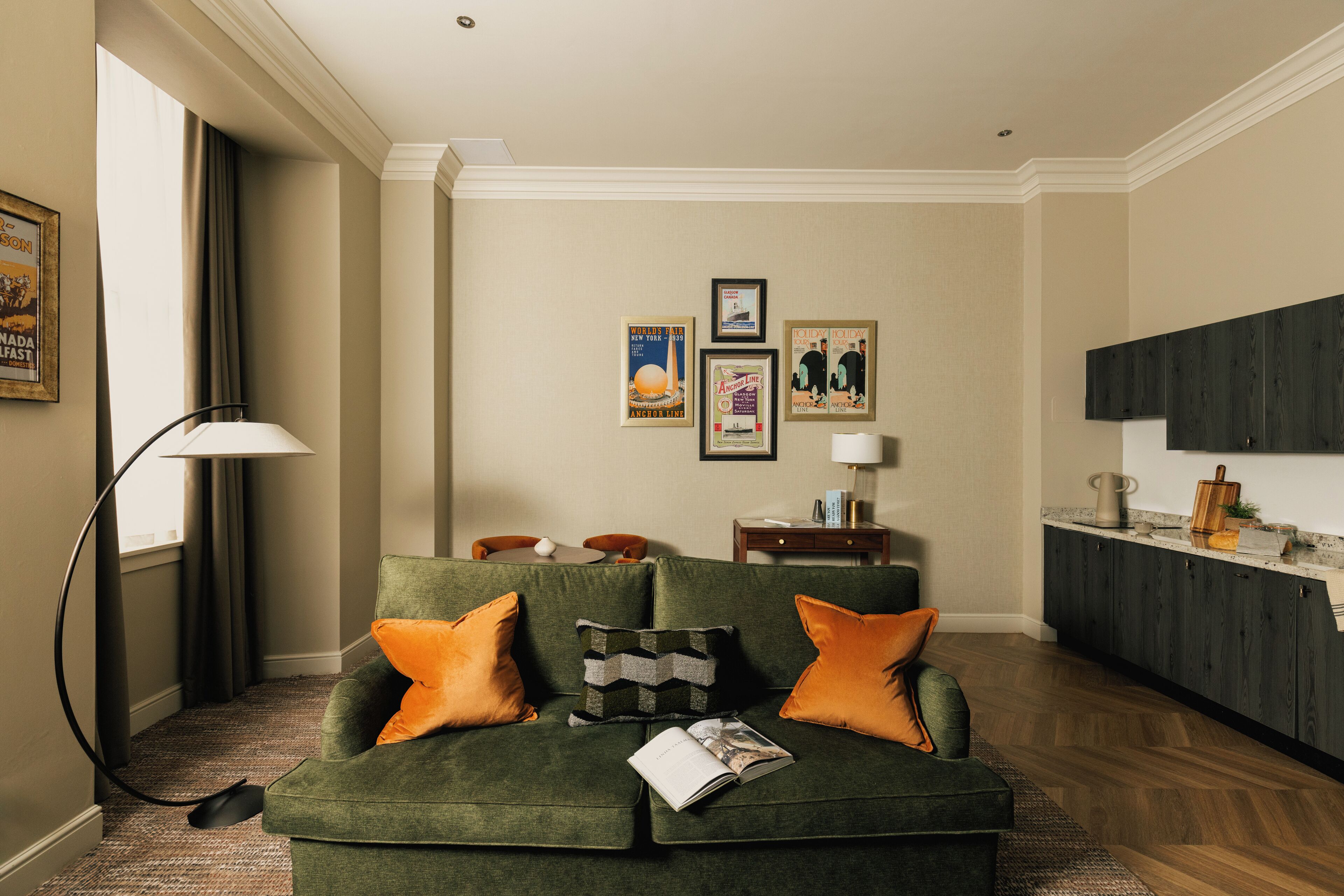 A living room with a green sofa, orange cushions, a lamp, and framed pictures on the wall.
