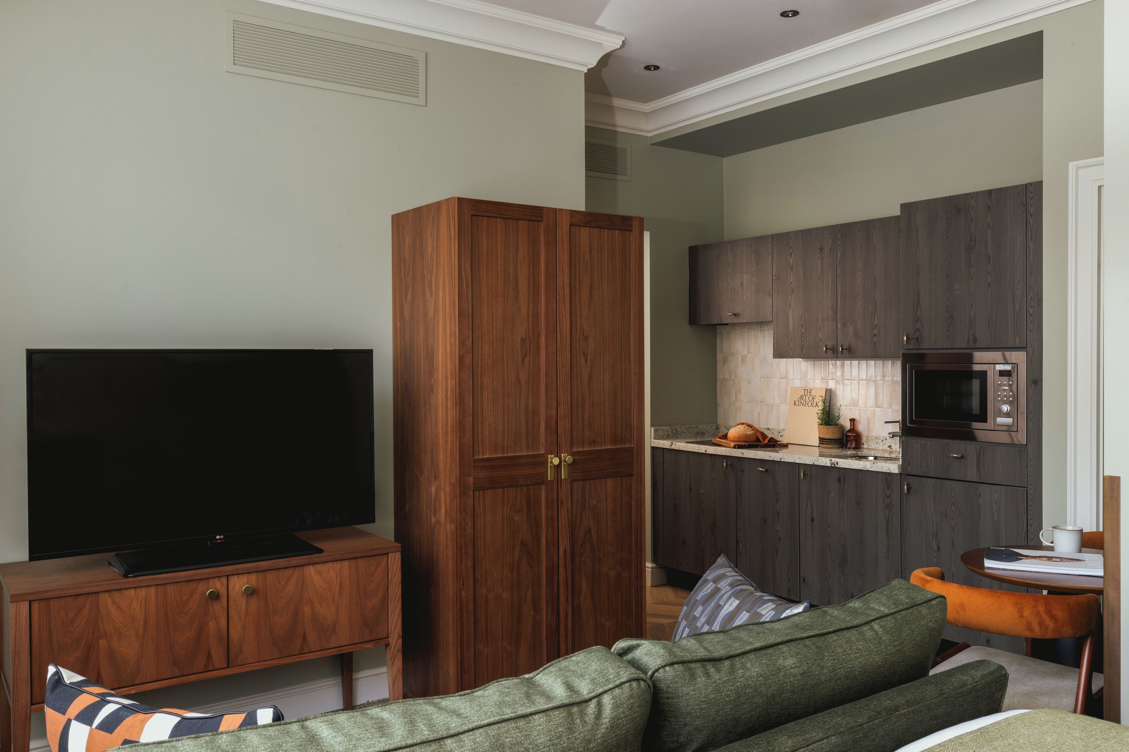 Ein Wohnzimmer mit Fernseher, Holzschrank und einem grünen Sofa.
