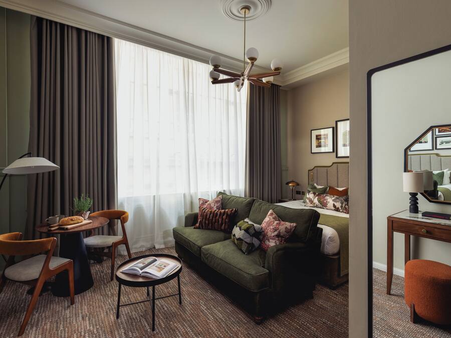 Una sala de estar moderna con un sofá verde, dos sillones, una mesa de centro y un comedor con una planta.