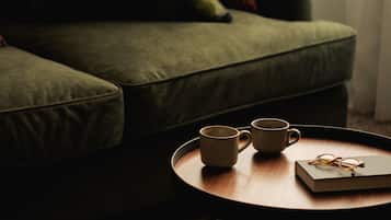 A green sofa with a pair of mugs and a book on a round wooden table.