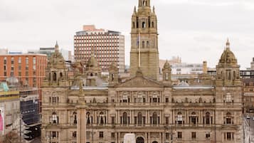 A historic building with a central dome and a tall tower, surrounded by a plaza with statues and a fountain.