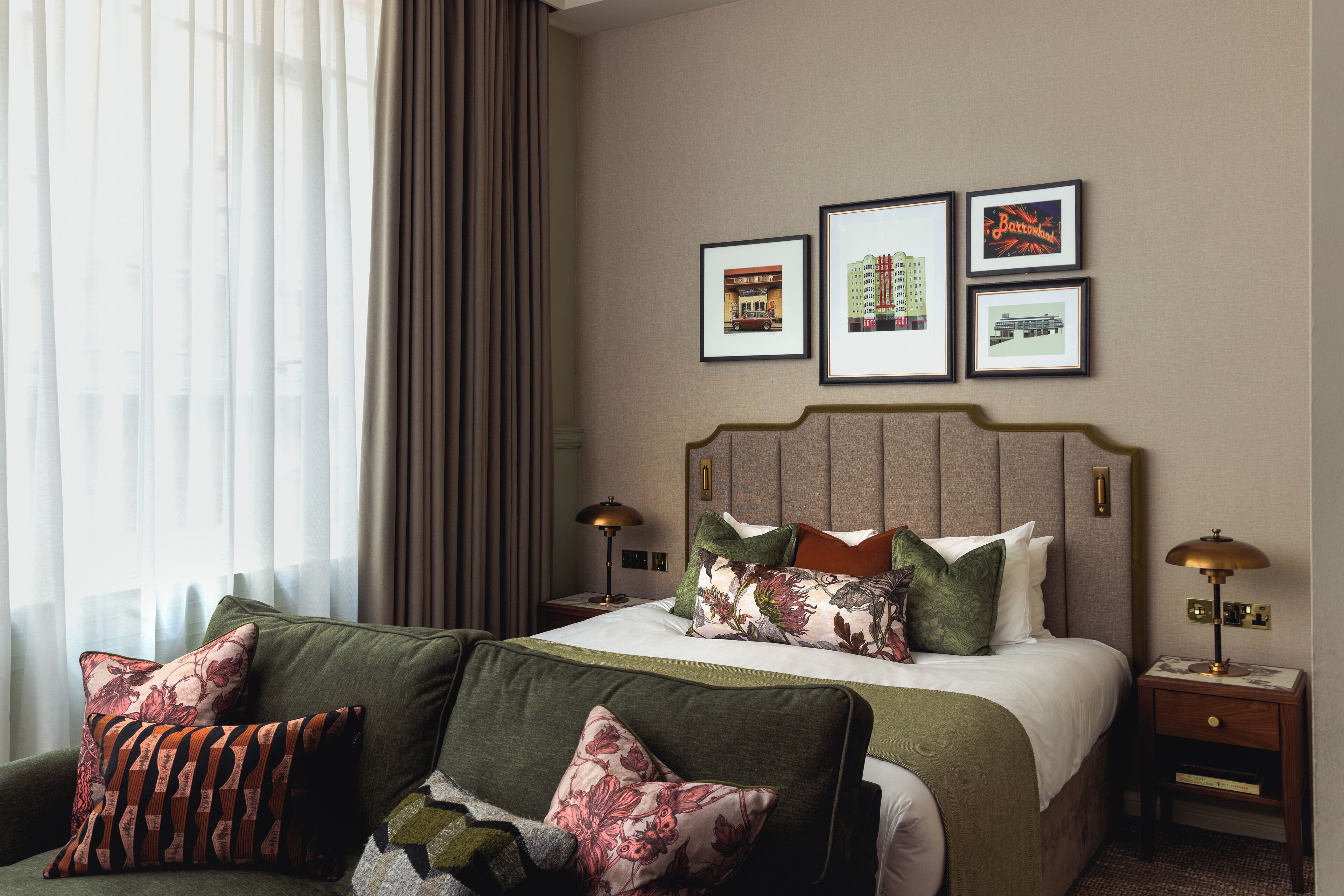 Una habitación de hotel con una cama, dos mesitas de noche, un sofá verde y un ventanal con cortinas.
