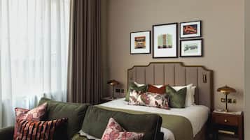 Una habitación de hotel con una cama, dos mesitas de noche, un sofá verde y un ventanal con cortinas.