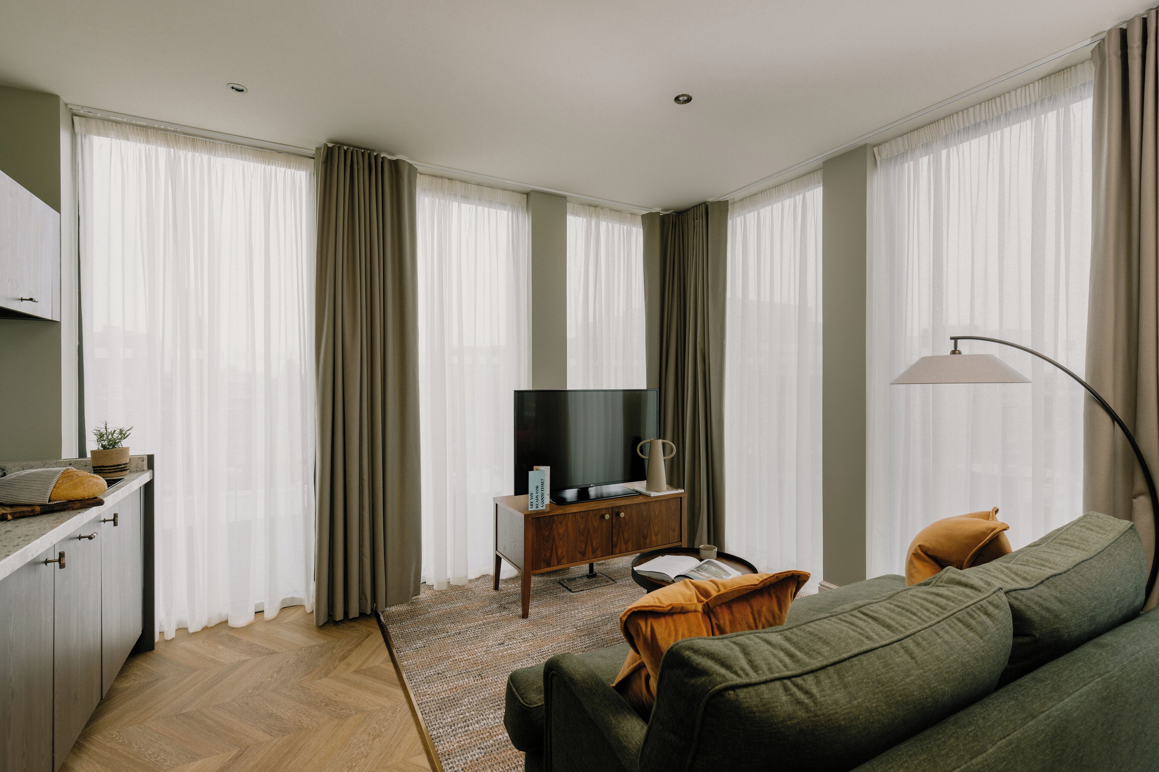 Uma sala de estar moderna com um sofá, uma televisão em um armário de madeira e uma luminária.