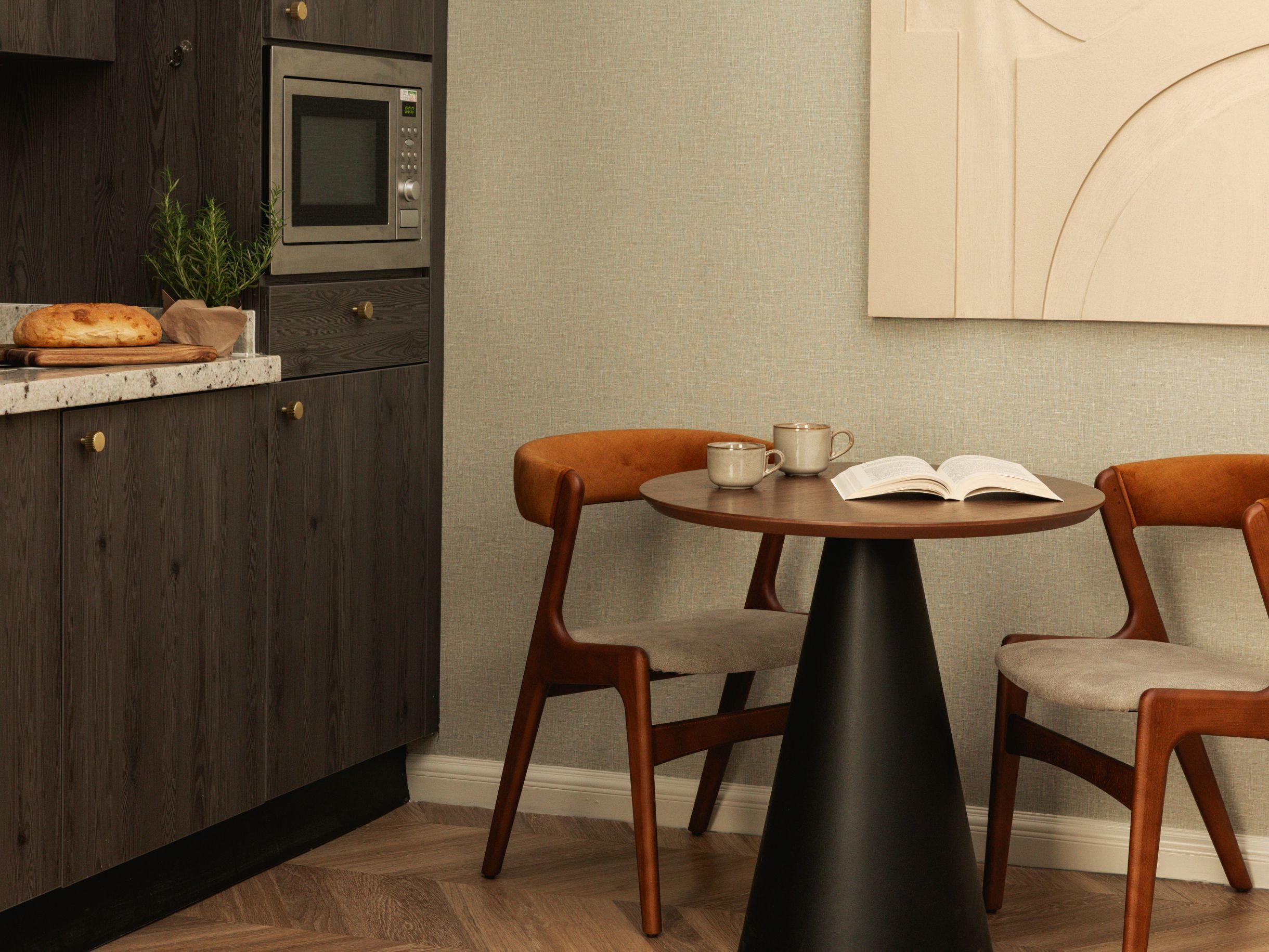 A modern kitchen with dark wooden cabinets, a built-in microwave, and a round table with two chairs.