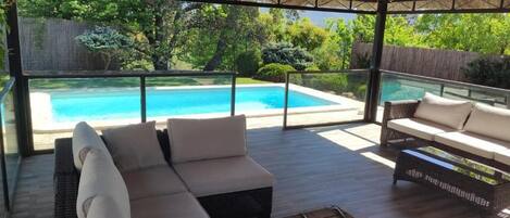 An outdoor patio with a pool, cushioned seating, and a wooden deck.