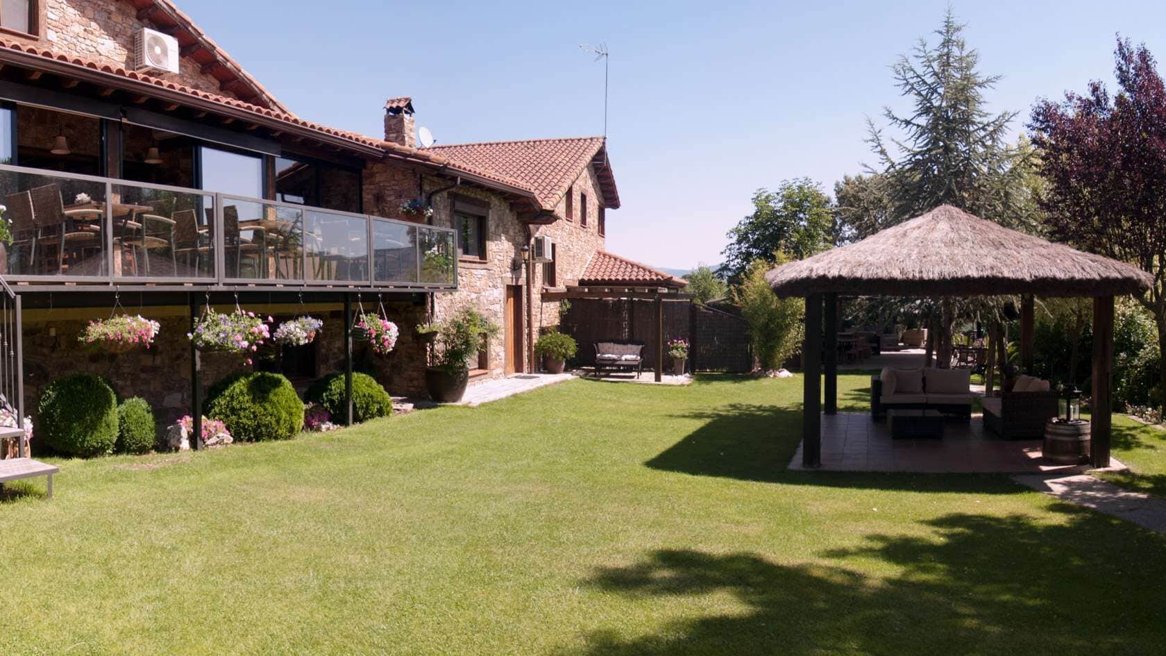 Un edificio de piedra con un patio, una zona de estar cubierta y un césped bien cuidado.