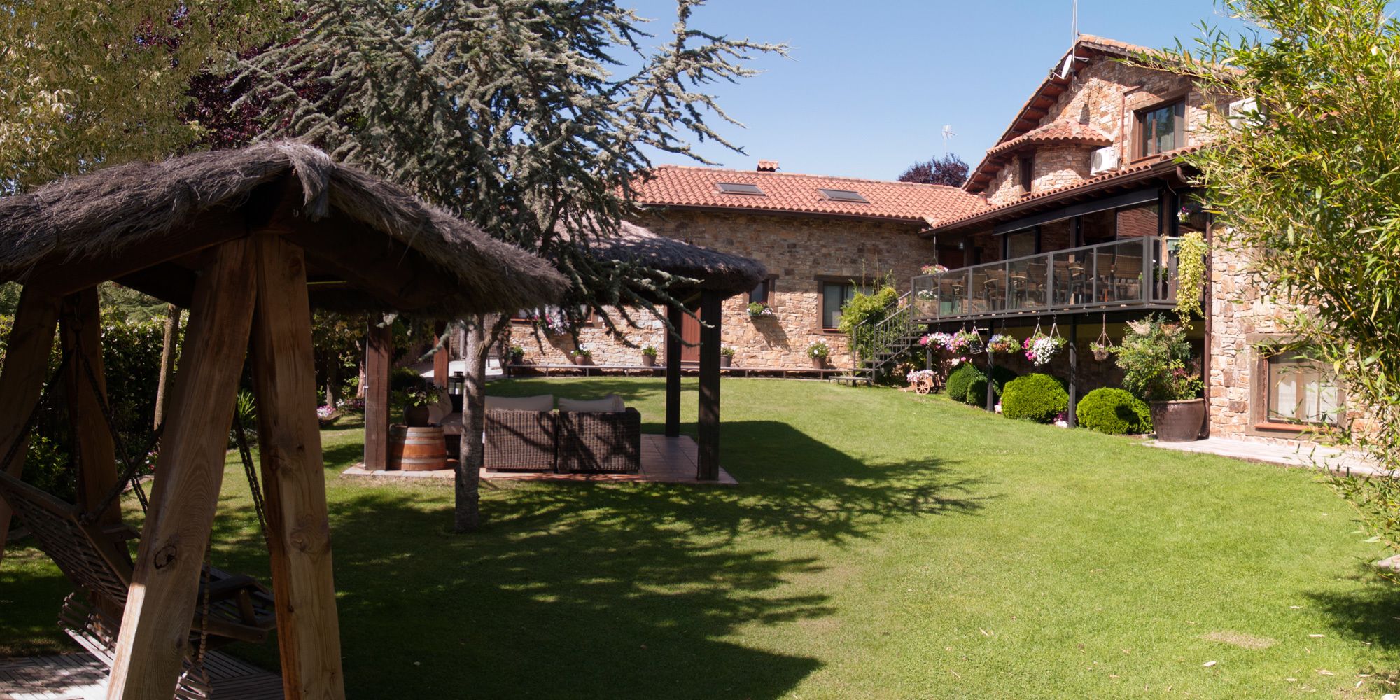 A stone building with a red-tiled roof, a wooden pergola, and a well-maintained lawn.