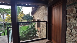 A balcony with a stone wall and a wooden door, overlooking a garden with a lawn and trees. - SAIKA Rural (Puentes Viejas)