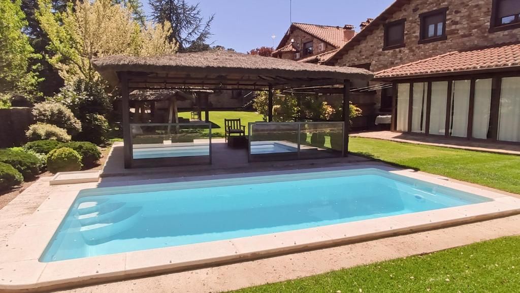 A rectangular swimming pool with a covered seating area and a house in the background.