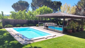 A rectangular swimming pool with a glass enclosure, a covered seating area with cushions, and potted plants around. - SAIKA Rural (Puentes Viejas)