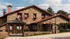 A stone building with a thatched roof entrance, multiple windows, and flower boxes. - SAIKA Rural (Puentes Viejas)