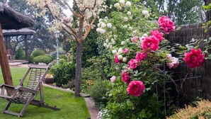 A garden with a wooden swing chair, a thatched-roof structure, and flowering plants. - SAIKA Rural (Puentes Viejas)
