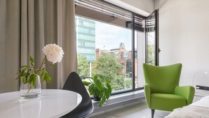 Ein modernes Zimmer mit einem großen Fenster, einem grünen Sessel, einem weißen Tisch und einem Blumentopf.