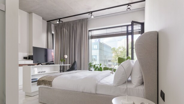 Ein modernes Schlafzimmer mit Bett, Fernseher, Schreibtisch und einem Fenster mit Vorhängen.