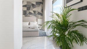 Ein modernes Schlafzimmer mit Wand in geometrischem Muster, einem großen Bett, einer Topfpflanze und Blick ins Freie.
