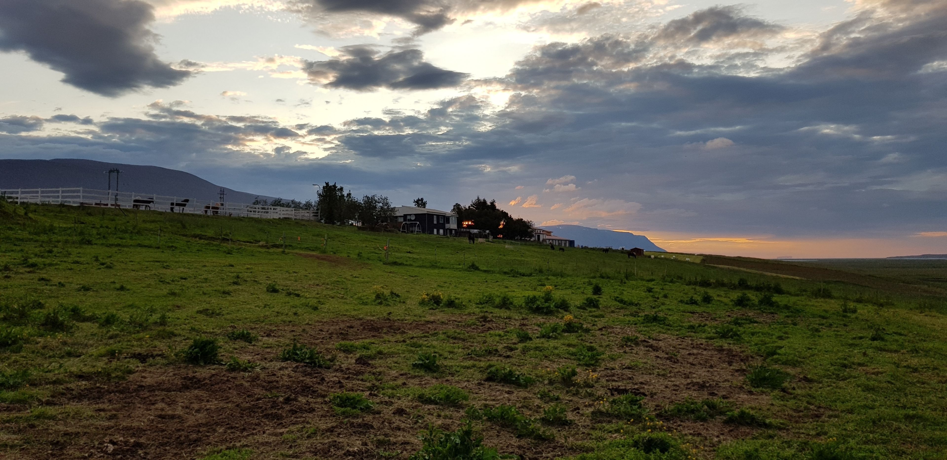Paisaje rural con una valla blanca, un edificio y una colina al fondo.