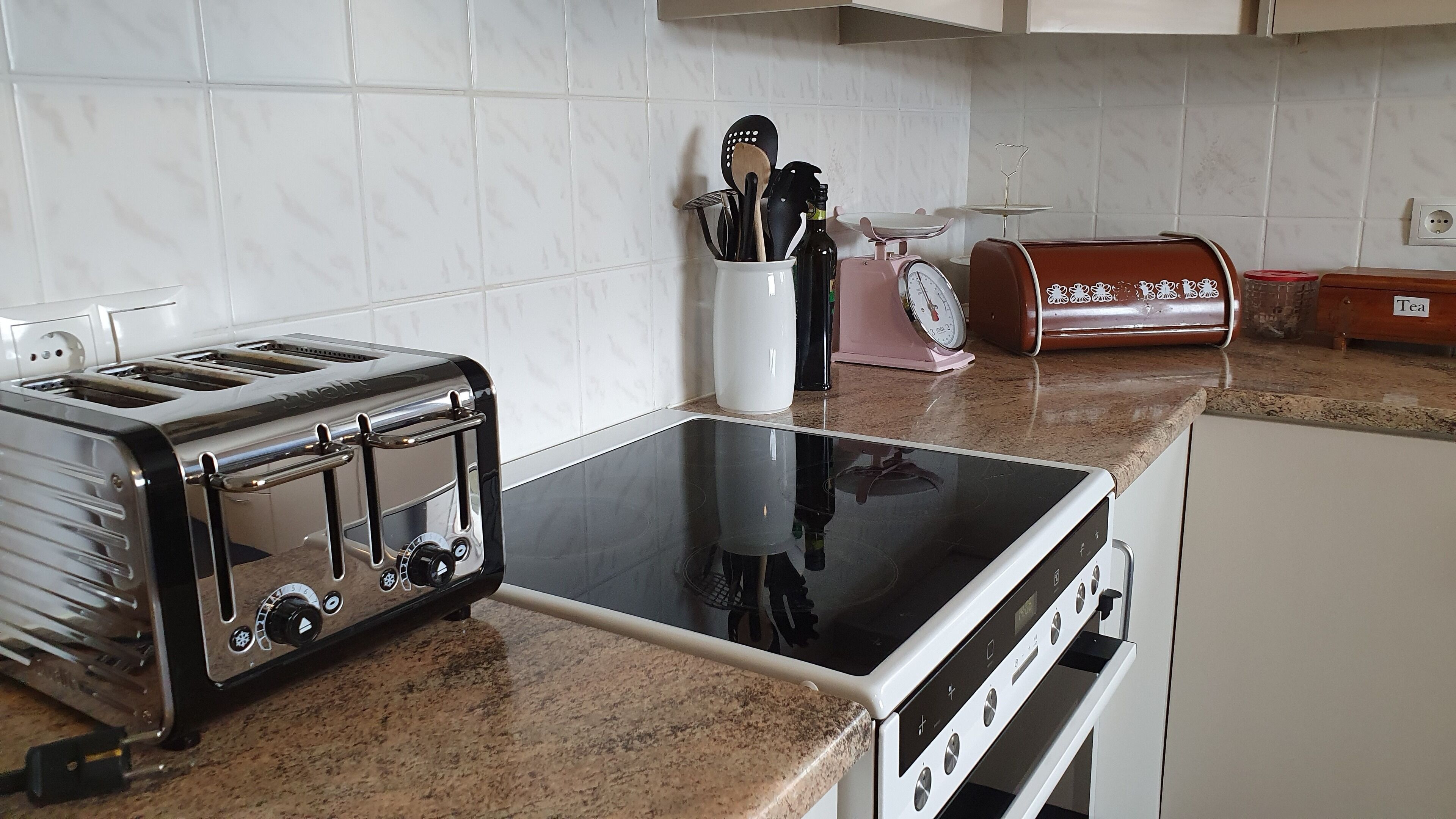 A kitchen with a black toaster, a white stove, and a red tea kettle.