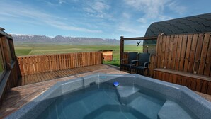 A hot tub with a view of mountains, wooden deck, and a patio area. - Karuna Guesthouse (Skagafjörour)