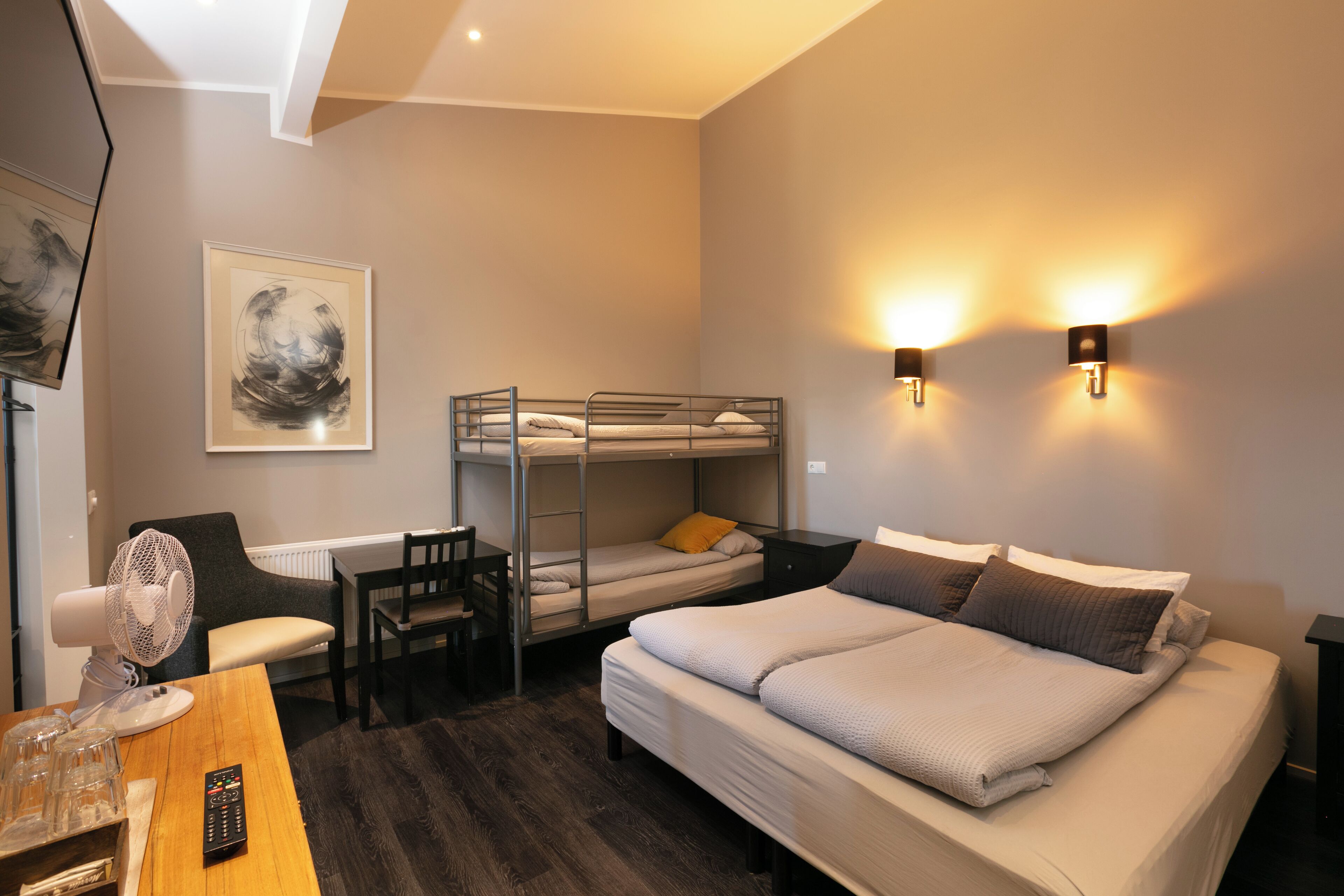 Habitación de hotel con una cama individual doble, un escritorio con silla, un ventilador y una cama con almohadas.