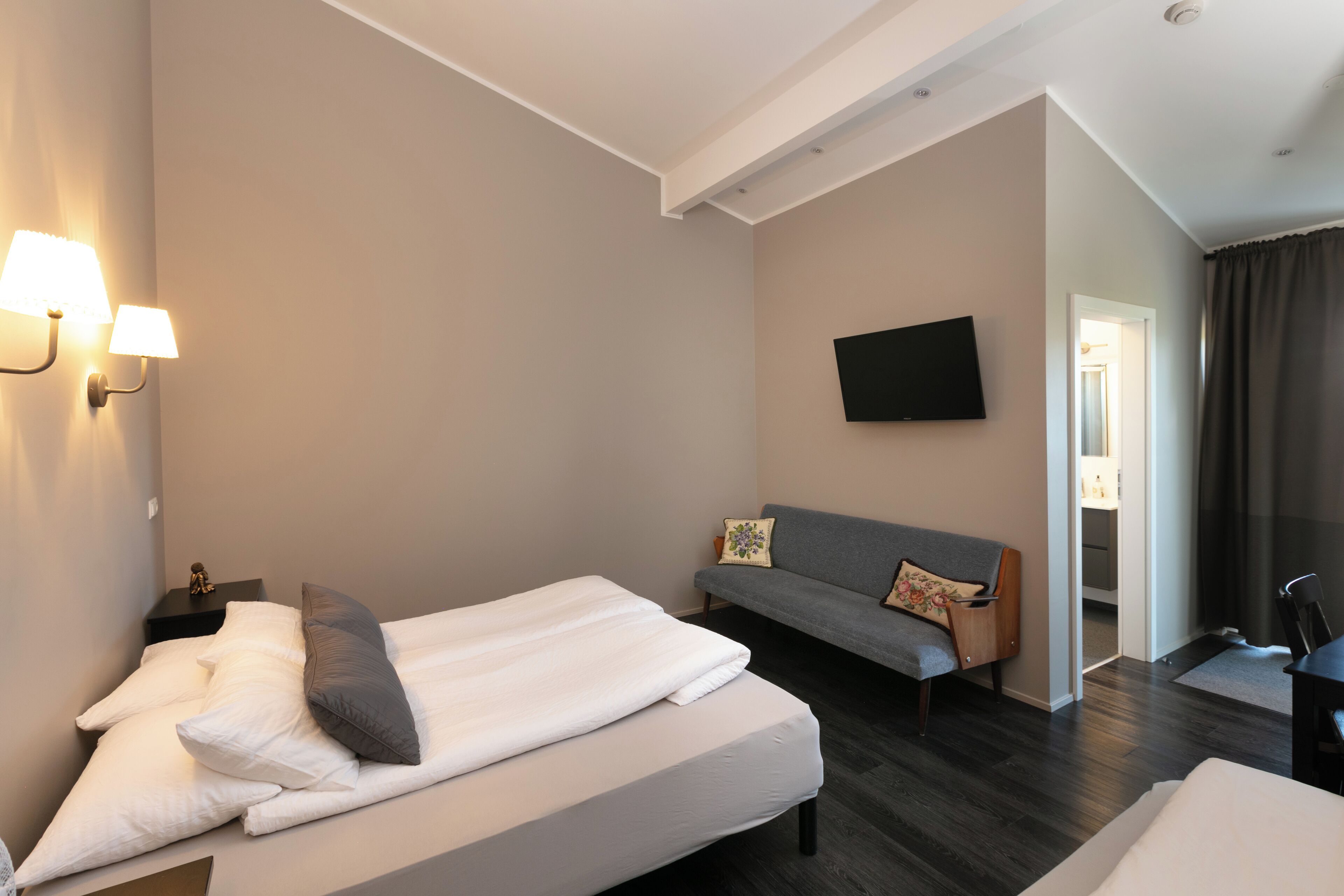A hotel room with a bed, a sofa, a TV mounted on the wall, and a desk with a chair.