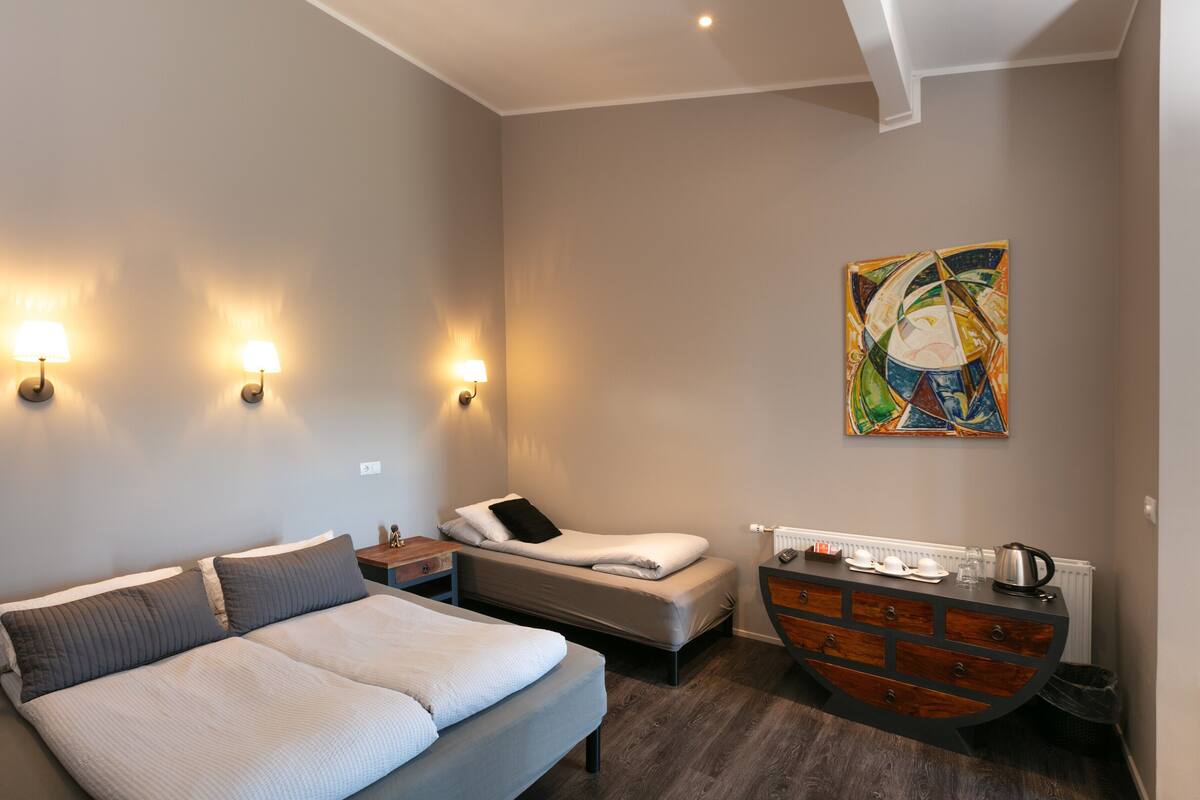 A hotel room with a large bed, a smaller bed, a dresser, and a painting on the wall.