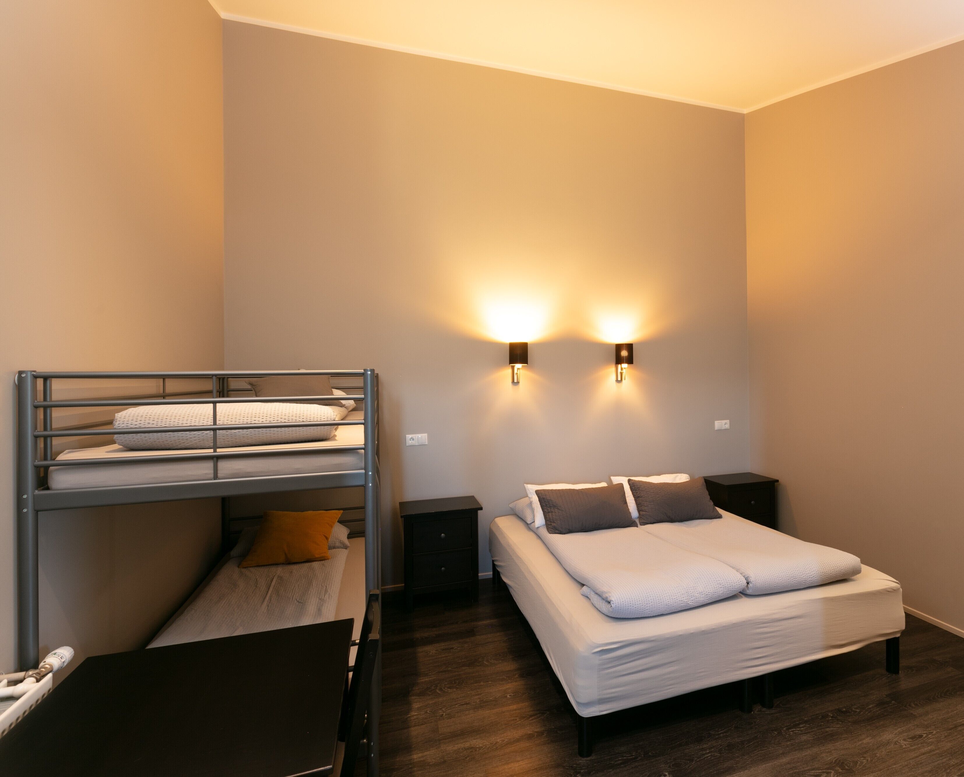 A bedroom with a bunk bed, a single bed, bedside tables, and wall-mounted lighting.