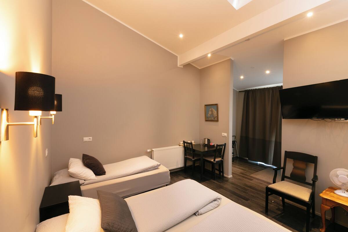 A hotel room with two beds, a desk, a chair, a TV, and a window with curtains.