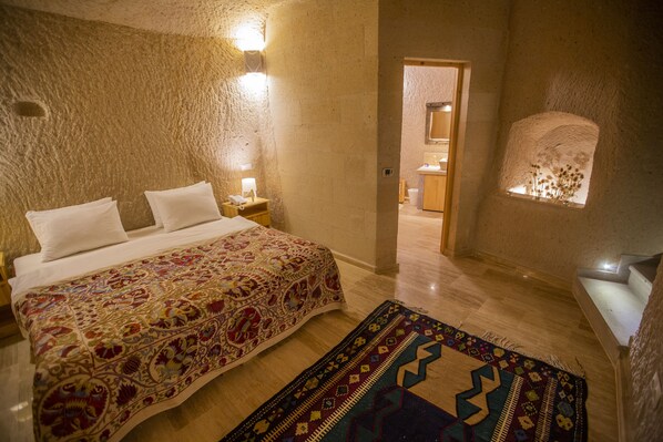 A bedroom with a large bed, a nightstand, a wall-mounted light, a window with a view, and a patterned rug. - Maze Of Cappadocia (Nevsehir)