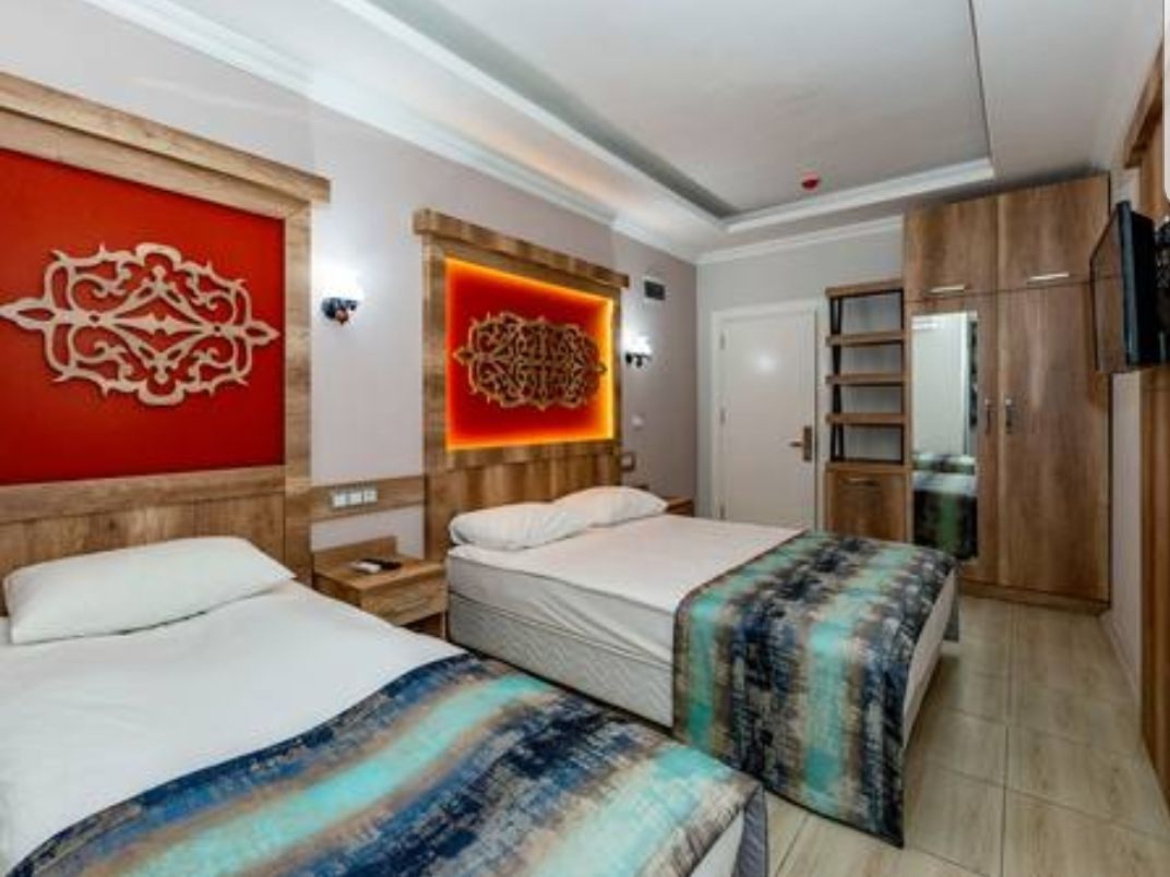 A hotel room with two beds, a wooden headboard, a red accent wall, and a television.
