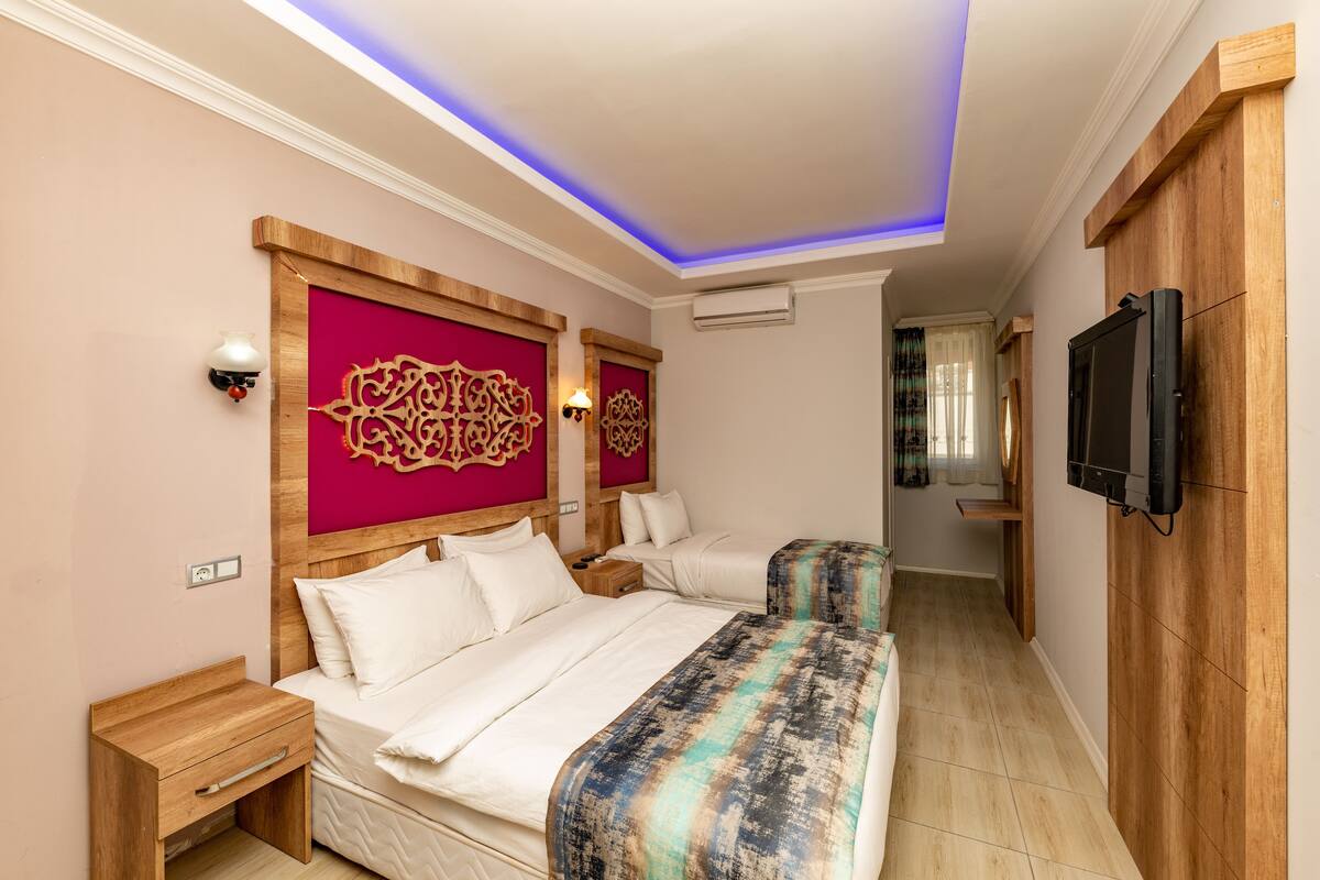 Quarto de hotel com duas camas, cabeceiras de madeira, uma TV de tela plana e um corredor que dá para outro quarto.