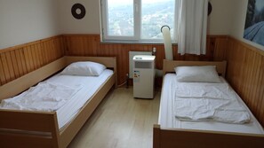 Quarto com duas camas de madeira, uma janela com vista para uma cidade e um ar condicionado fixado na parede.