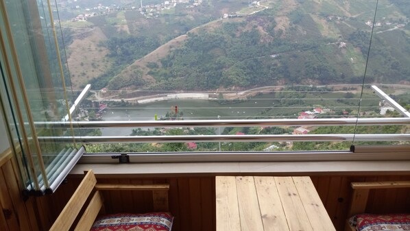 A balcony with a wooden bench and a view of a river and hills.