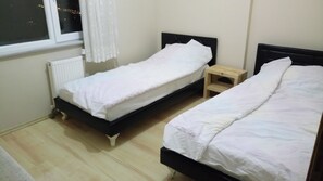 Quarto pequeno e limpo com duas camas de solteiro, janela com cortinas e radiador.