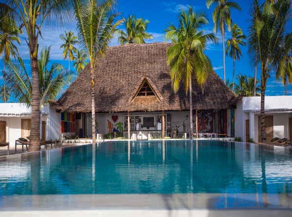 Um resort com piscina, palmeiras e um edifício com telhado de palha.