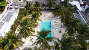 Vista aérea de um resort com uma piscina central, rodeada por palmeiras e espreguiçadeiras.