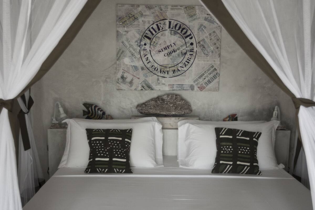 Una cama con dosel, ropa de cama blanca, almohadas estampadas y una pared con diseño circular.
