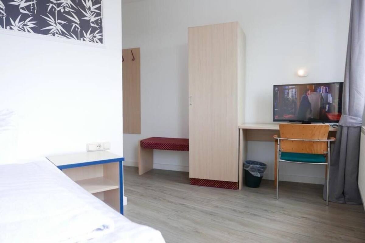 Huoneessa on sänky, työpöytä tuolilla, vaatekaappi ja televisio.
