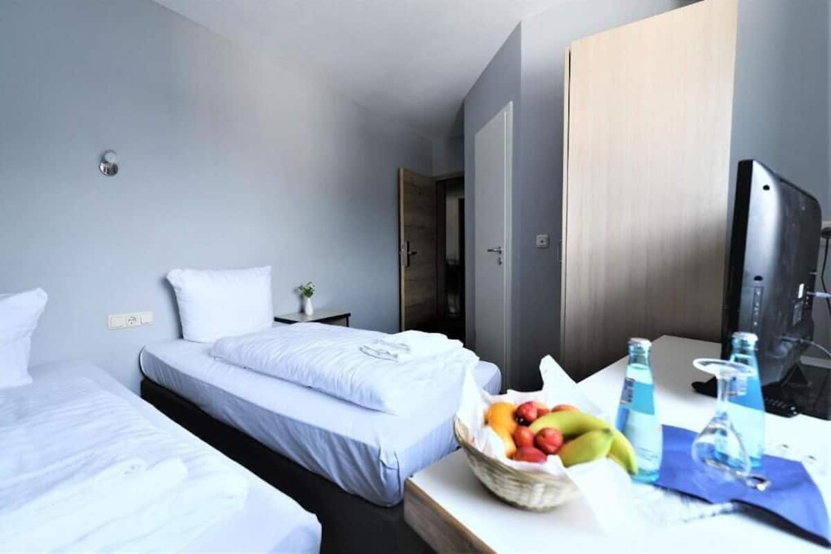 Hotellihuone, jossa on kaksi sänkyä, työpöytä tietokoneella, televisio ja hedelmäkori.