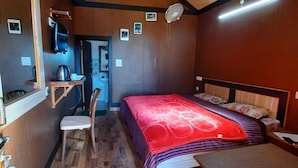 Een compacte slaapkamer met een bed, een klein tafeltje, een stoel en een houten plafond.