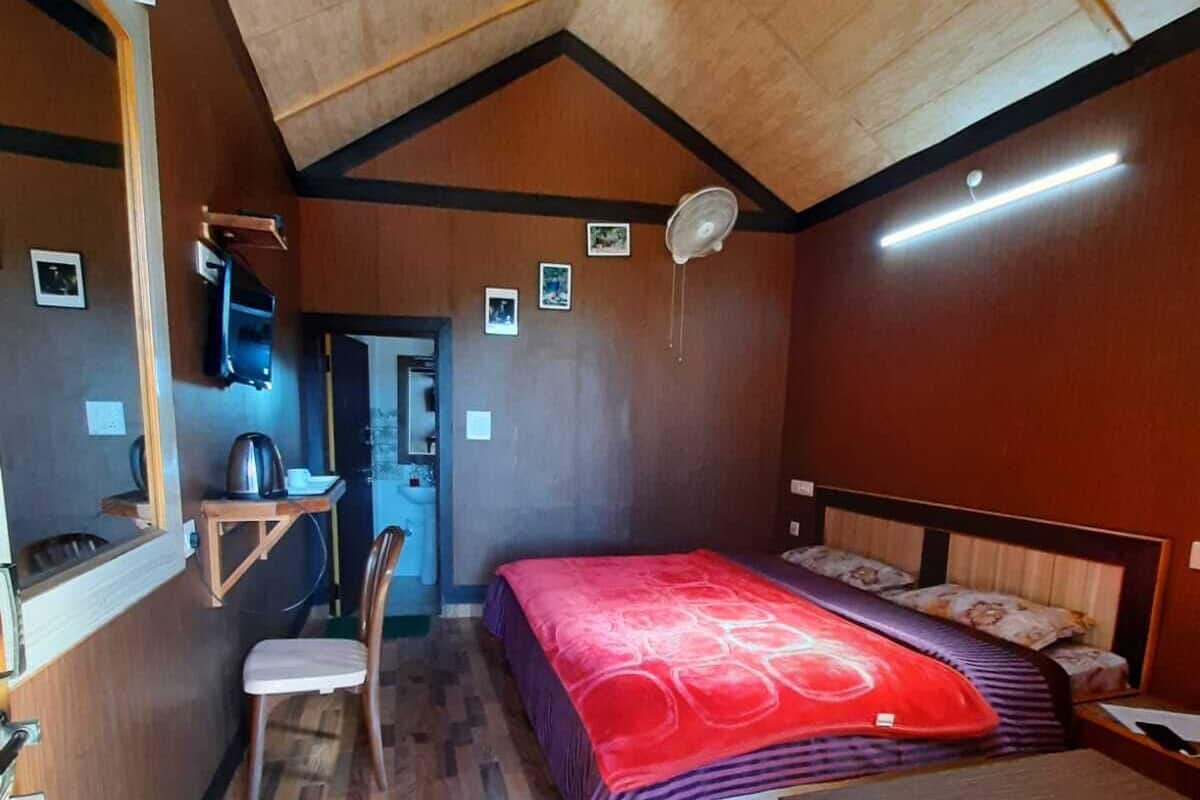 A compact bedroom with a bed, a small table, a chair, and a wooden ceiling.