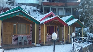Een rij houten chalets met bakstenen muren en sneeuw bedekte daken, elk met een veranda en zitplaatsen.