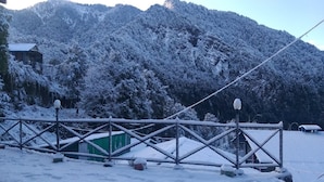Een berglandschap bedekt met sneeuw, met een houten hek en een klein groen gebouw.