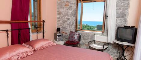 A bedroom with a bed, a television, a stone wall, and a window with a view.
