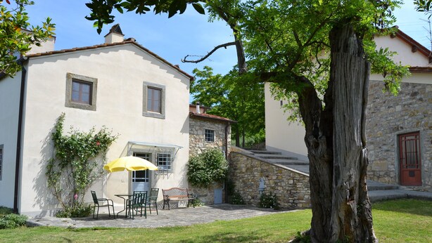 A building with a stone facade, a large tree in the foreground, and a patio area with outdoor seating. - Agriturismo Montereggi (Fiesole)