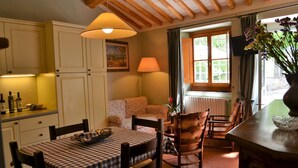 A cozy dining area with a checkered tablecloth, wooden chairs, and a lamp. There is a sofa with a floral pattern in the background, and a window with curtains. - Agriturismo Montereggi (Fiesole)