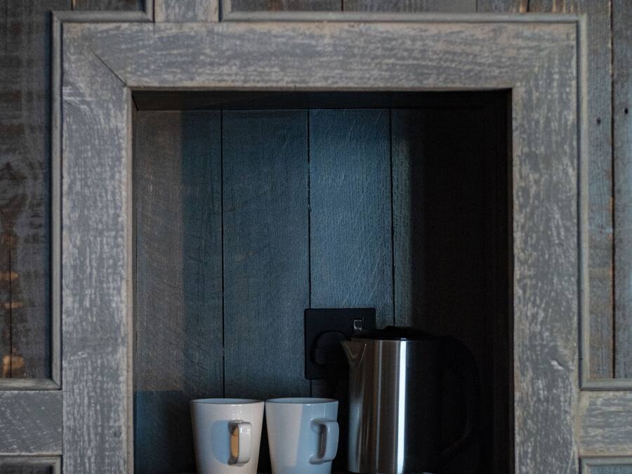 A rustic wooden wall with a built-in shelf containing a stainless steel coffee pot and two white mugs.